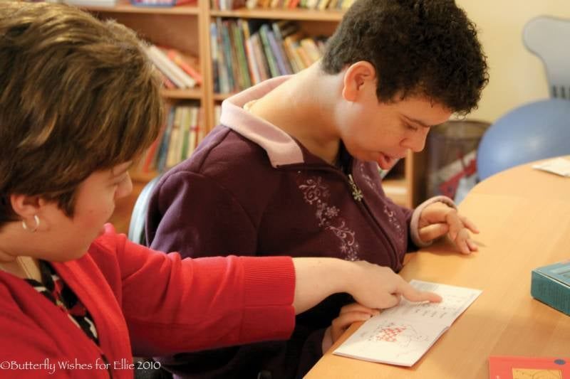 a woman in a red sweater is helping a boy with a piece of paper