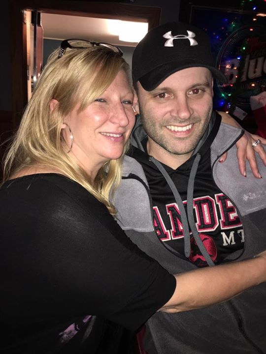 A man wearing an under armour hat is hugging a woman