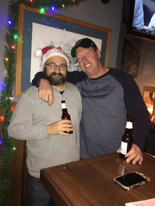 Two men posing for a picture with one wearing a santa hat