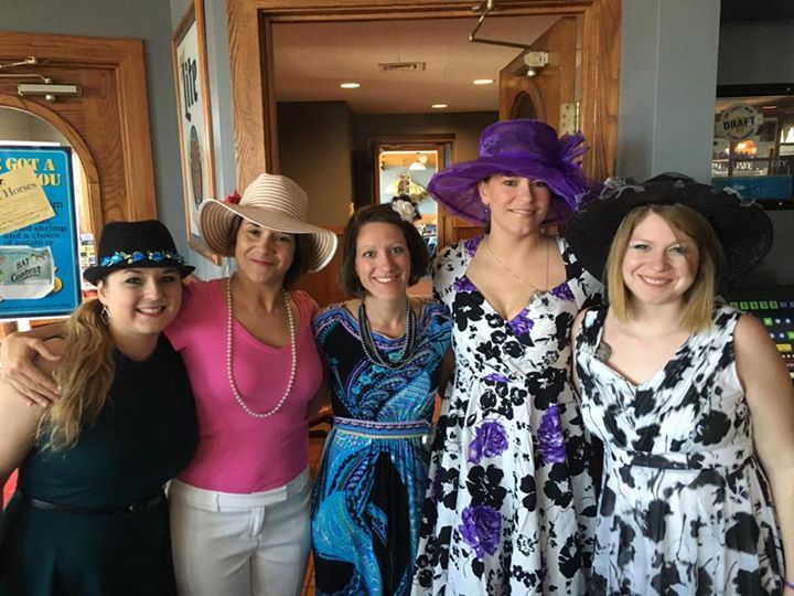 A group of women wearing hats and dresses are posing for a picture.