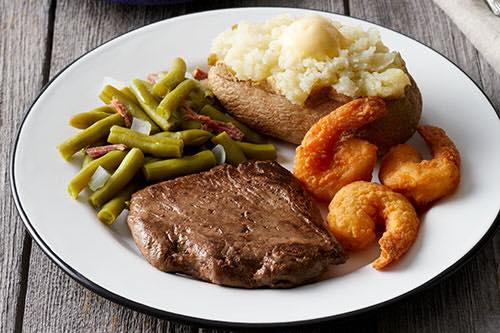A white plate topped with steak , shrimp , green beans and a baked potato.