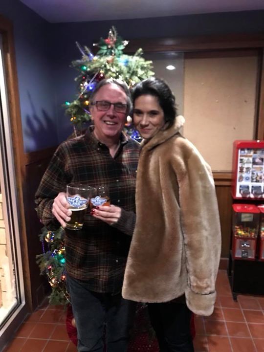 A man and a woman are posing for a picture in front of a christmas tree.