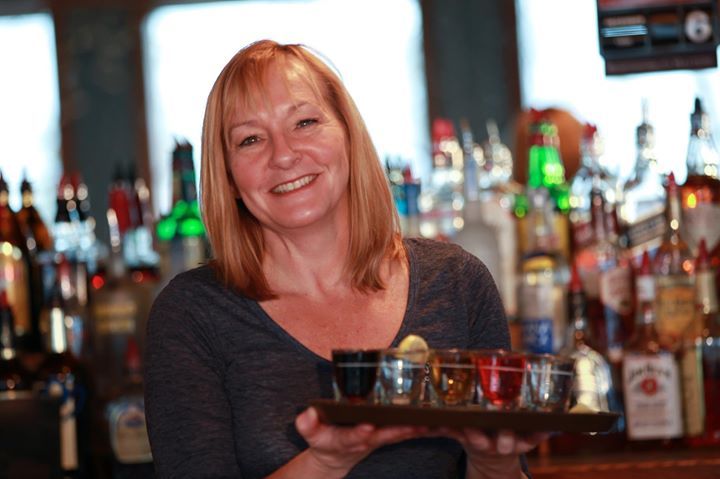 A woman holding a tray of shot glasses in front of a bar