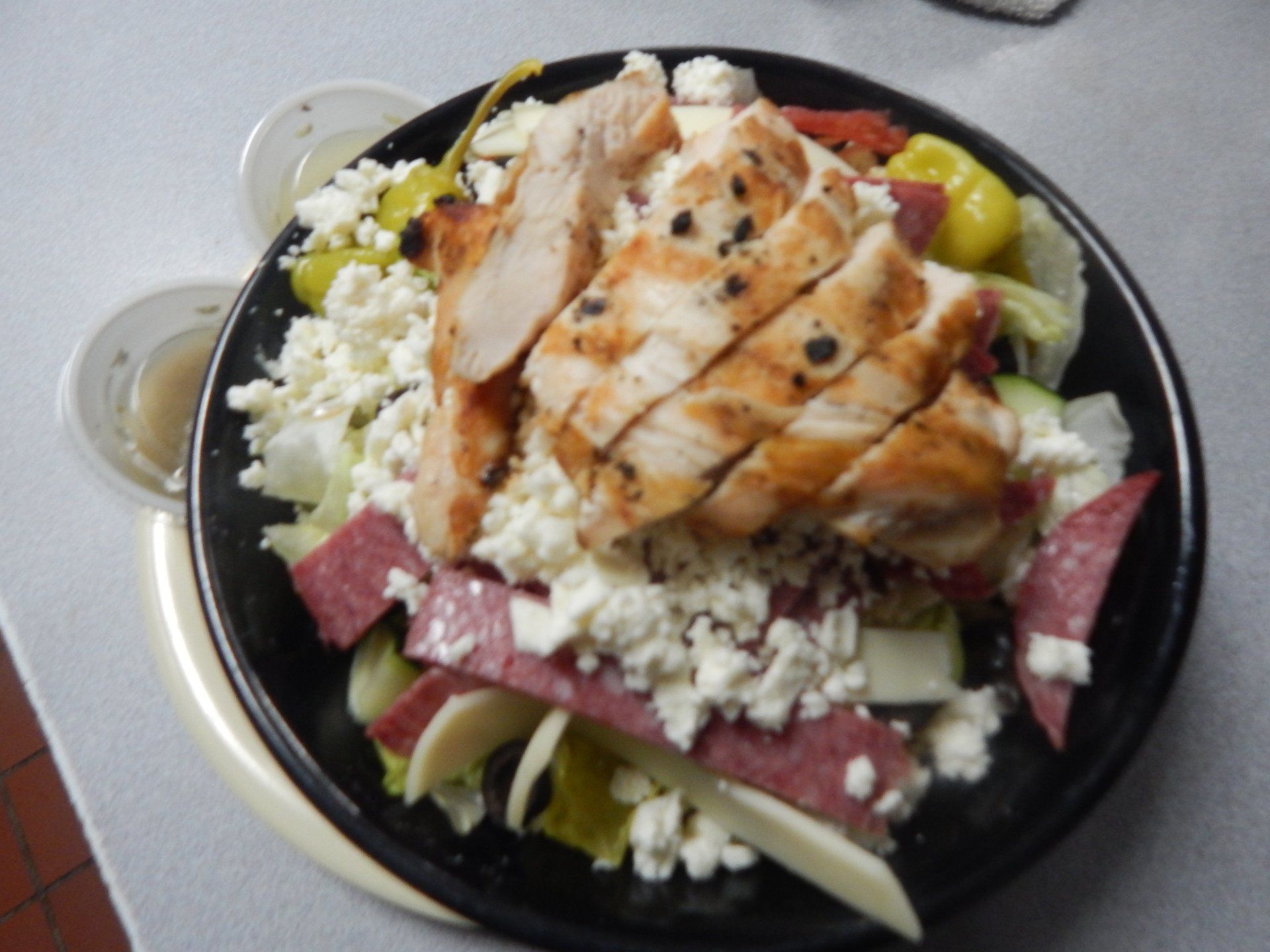 A salad with chicken and cheese on a black plate