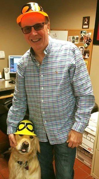 A man standing next to a dog wearing an orange hat