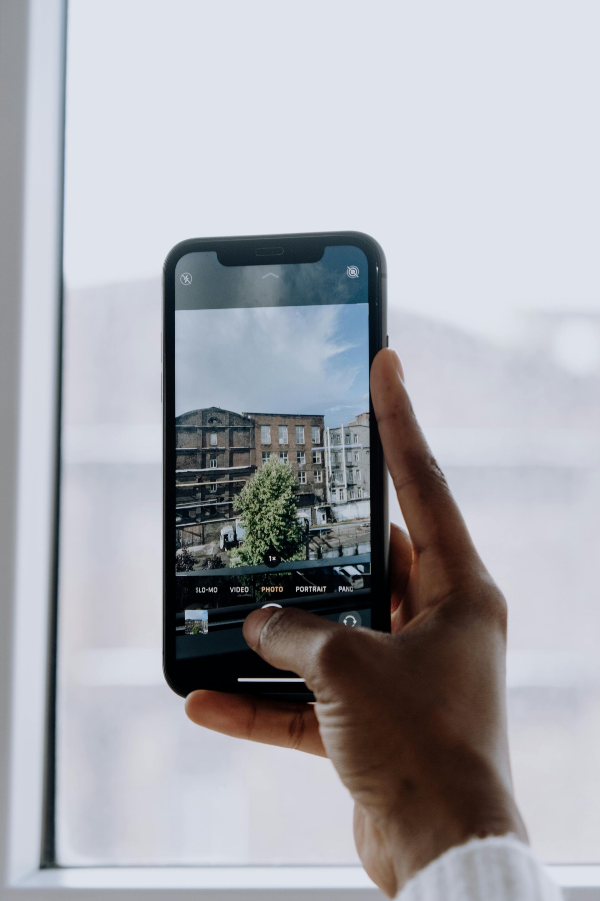 Mano sosteniendo un teléfono, tomando una fotografía de edificios a través de una ventana.