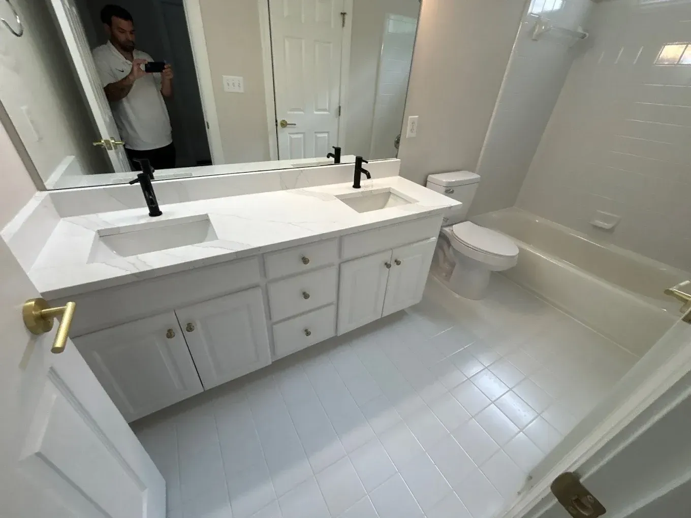 Bathroom with white vanity, black faucets, and a person reflected in the mirror taking a photo.