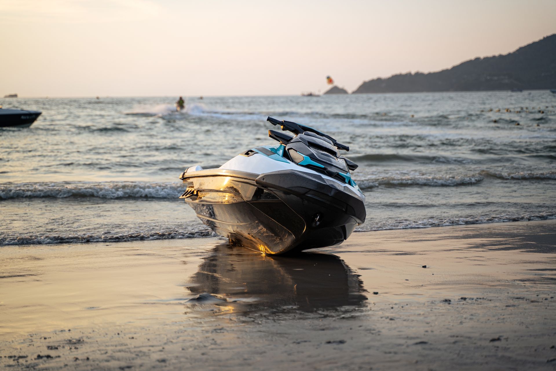 Jet ski beached on a sandy shore at sunset, waves in background.