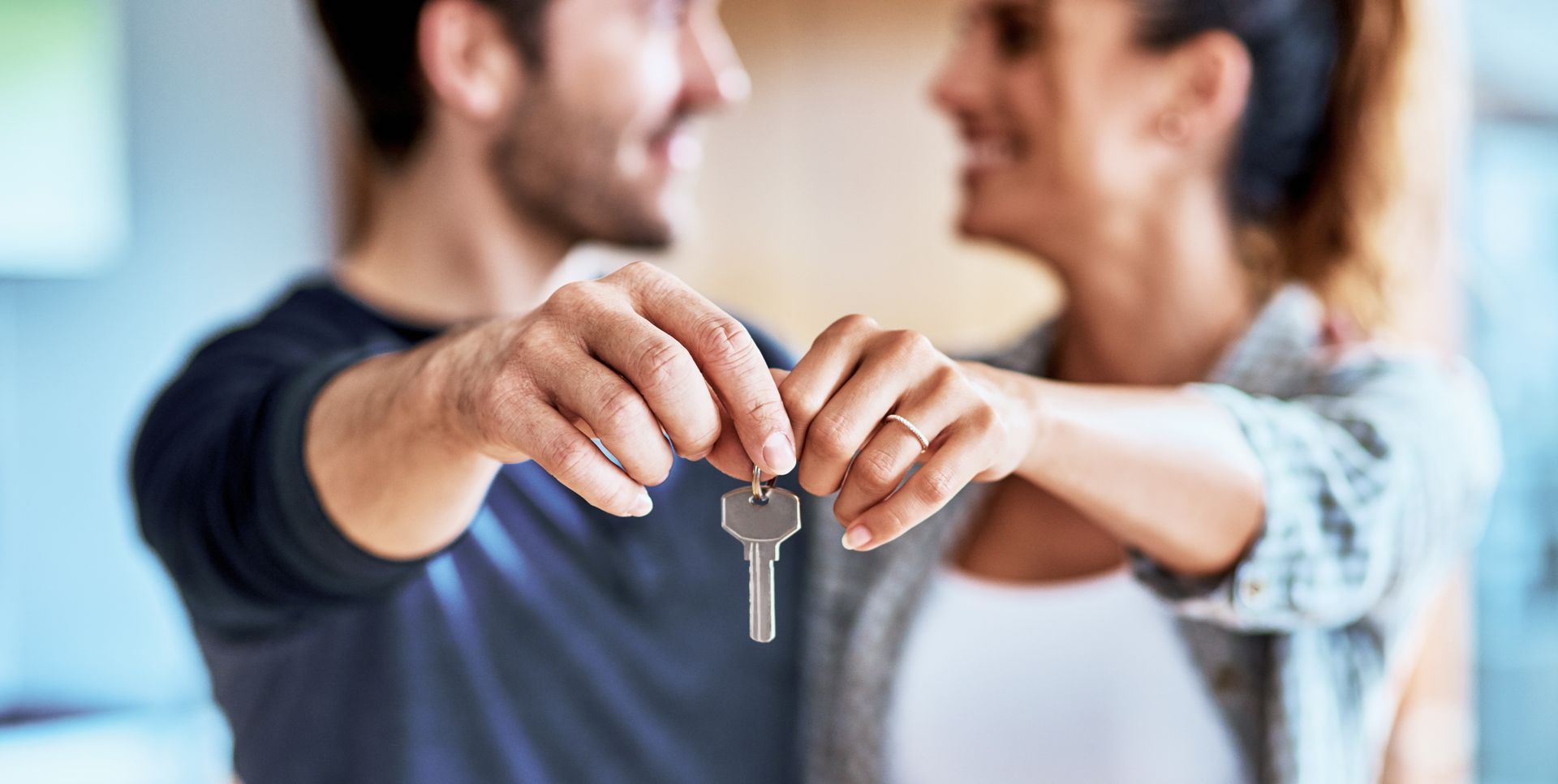 Couple holding house keys, smiling, in front of a blurred background.
