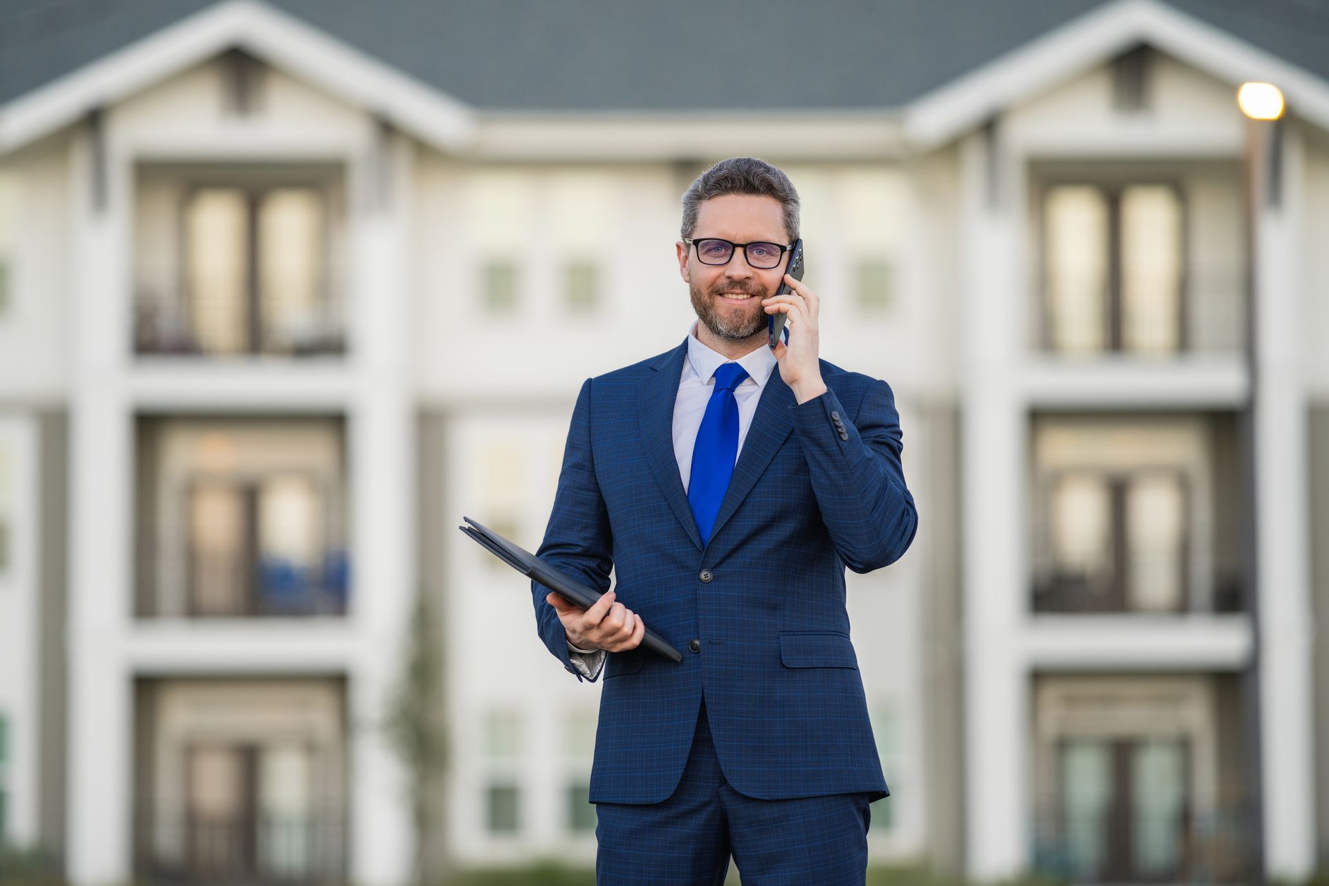Real estate agent on phone holding tablet, standing in front of building.