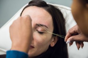 A woman is getting her eyebrows threaded by a woman.