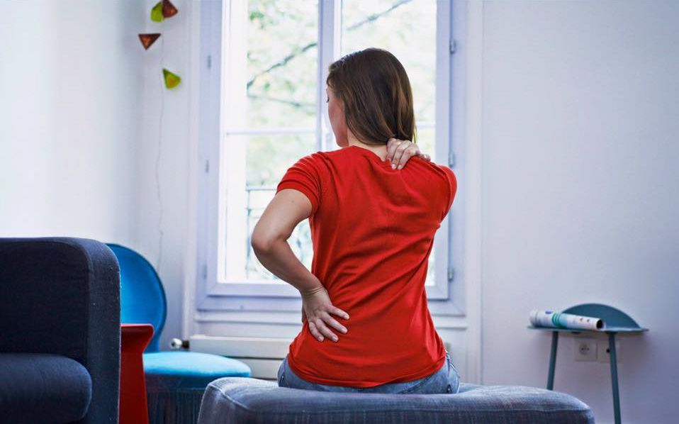 A woman is sitting on a couch holding her back in pain