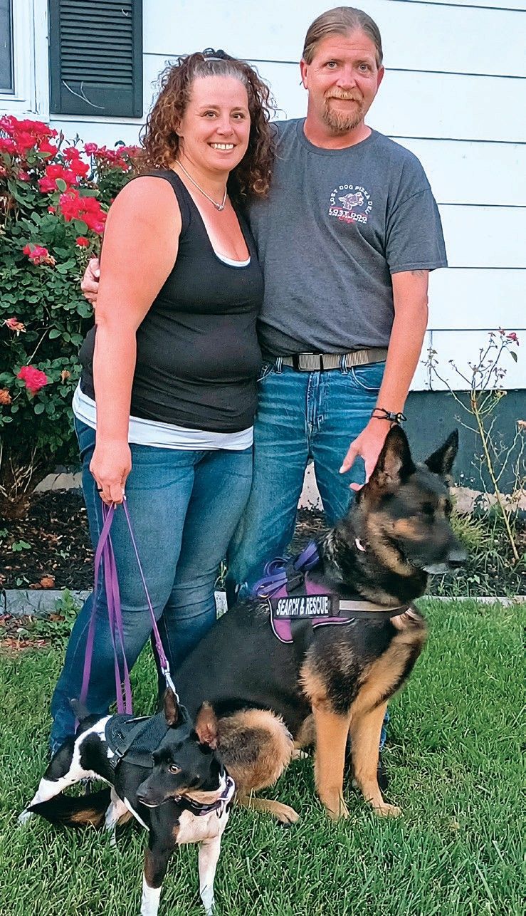 A man and a woman are posing for a picture with their dogs.