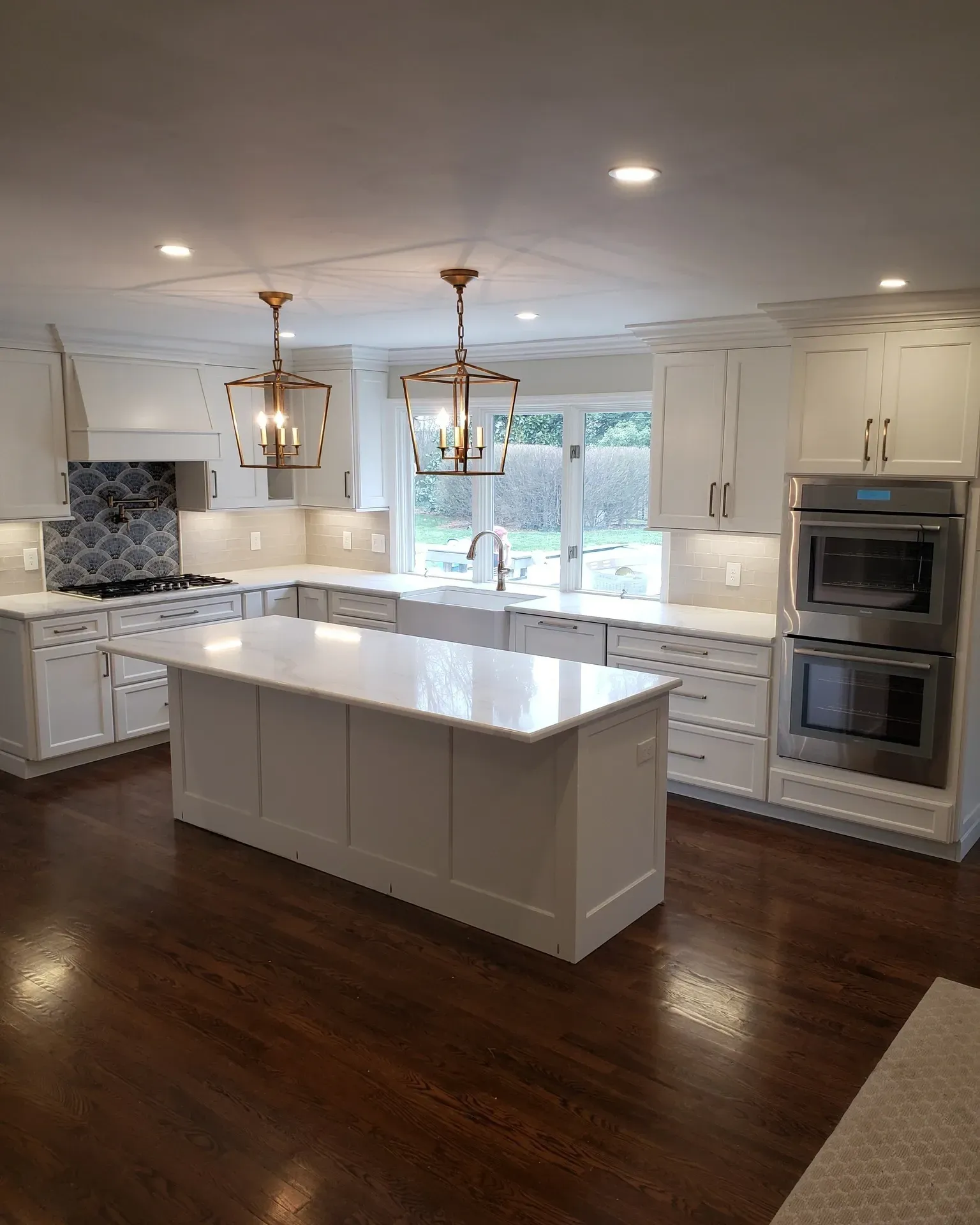 Modern white kitchen with island, dark wood floors, and gold pendant lights.