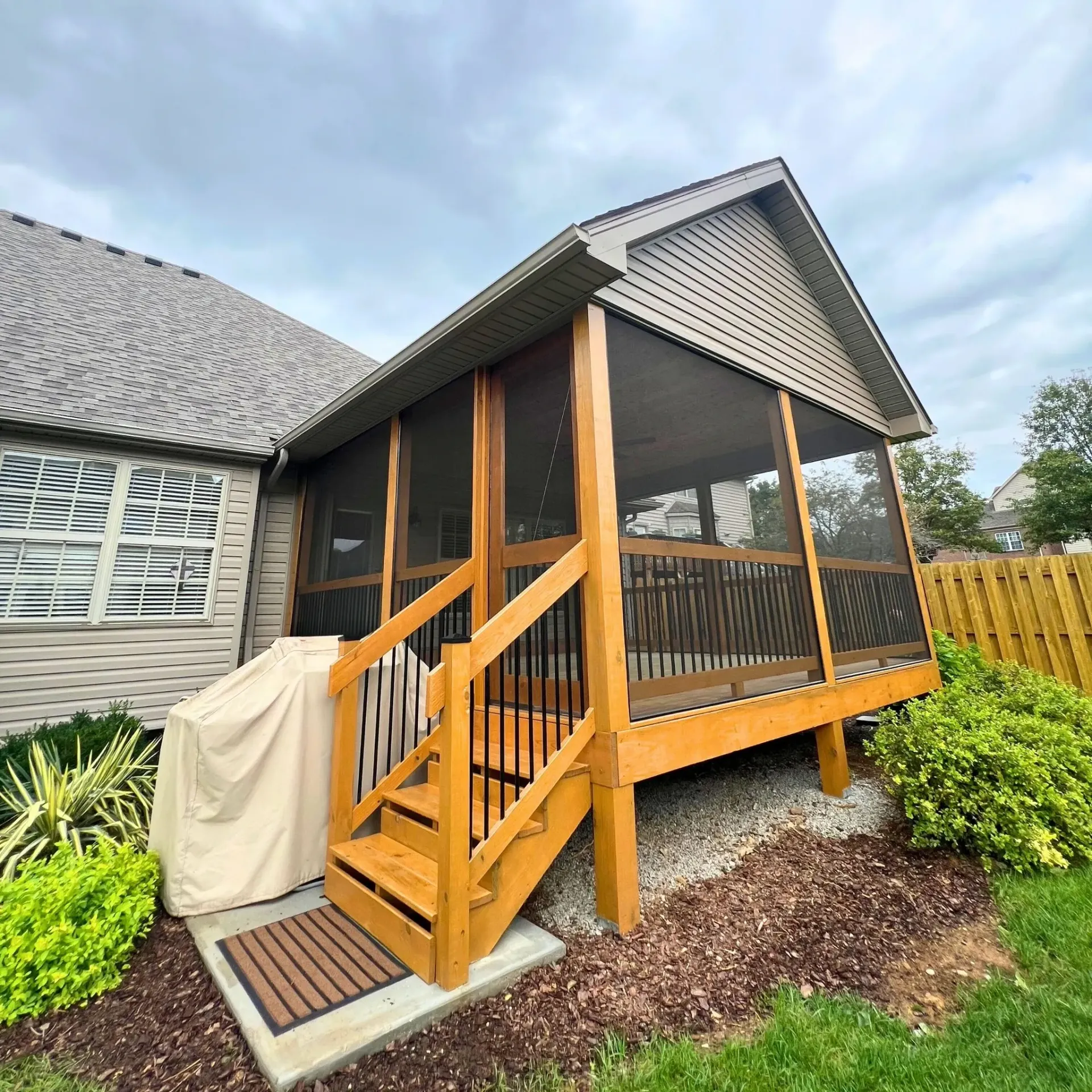 Screened-in porch with wooden steps, a gabled roof, and a beige grill cover.