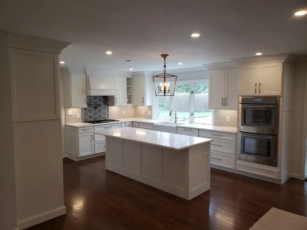 Bright, white kitchen with island, cabinets, oven, and dark wood floors.