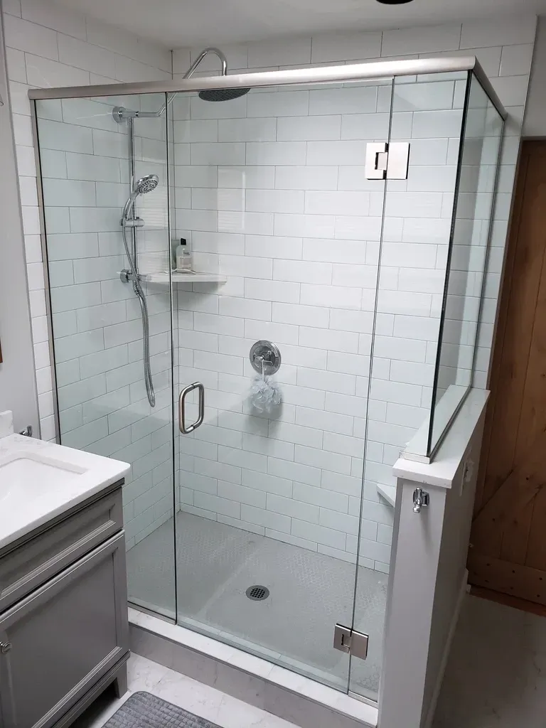 Modern glass shower with white subway tiles, silver fixtures, and gray vanity.