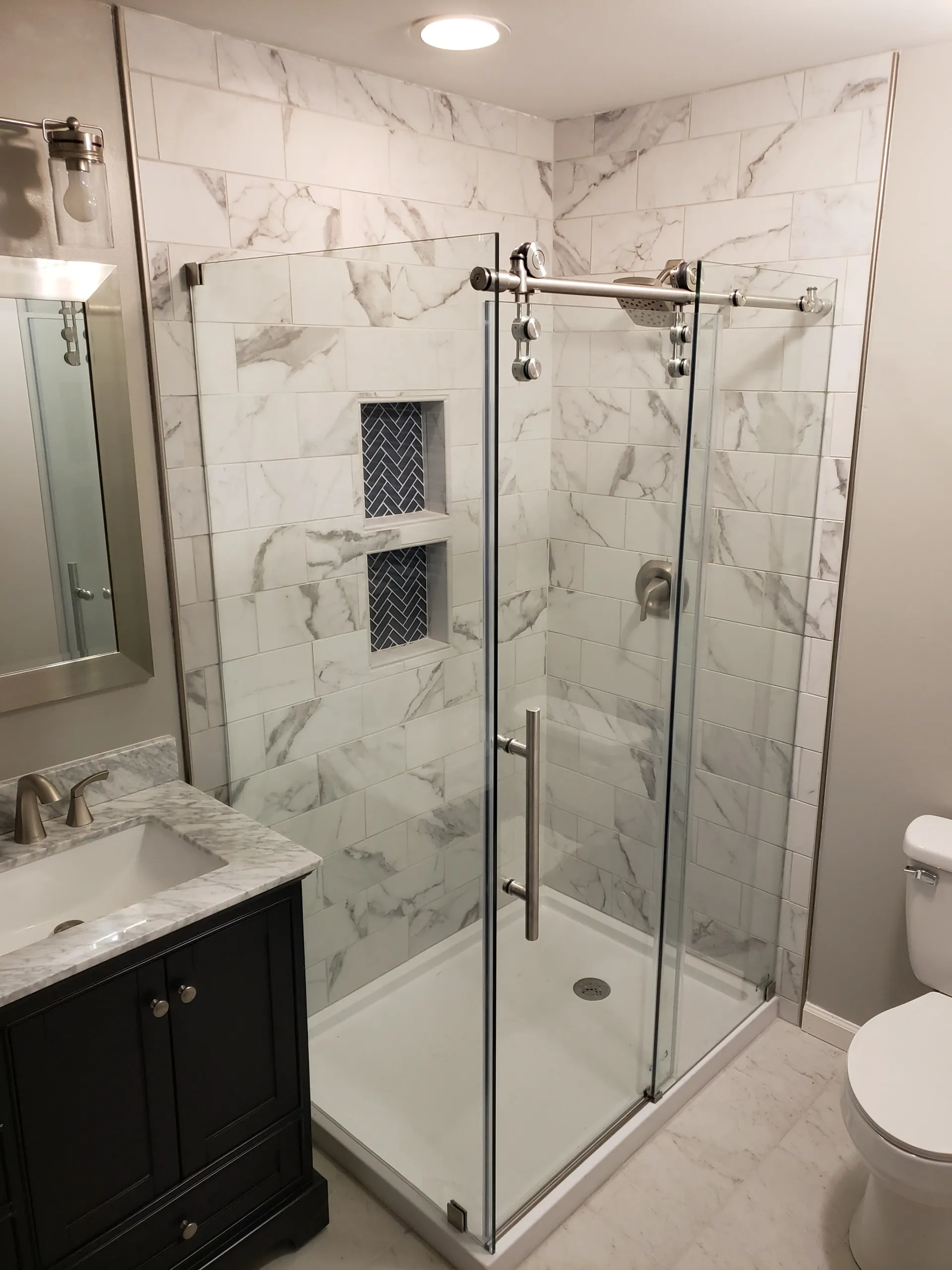 Modern bathroom with marble-look tile, glass shower door, black vanity, and white toilet.