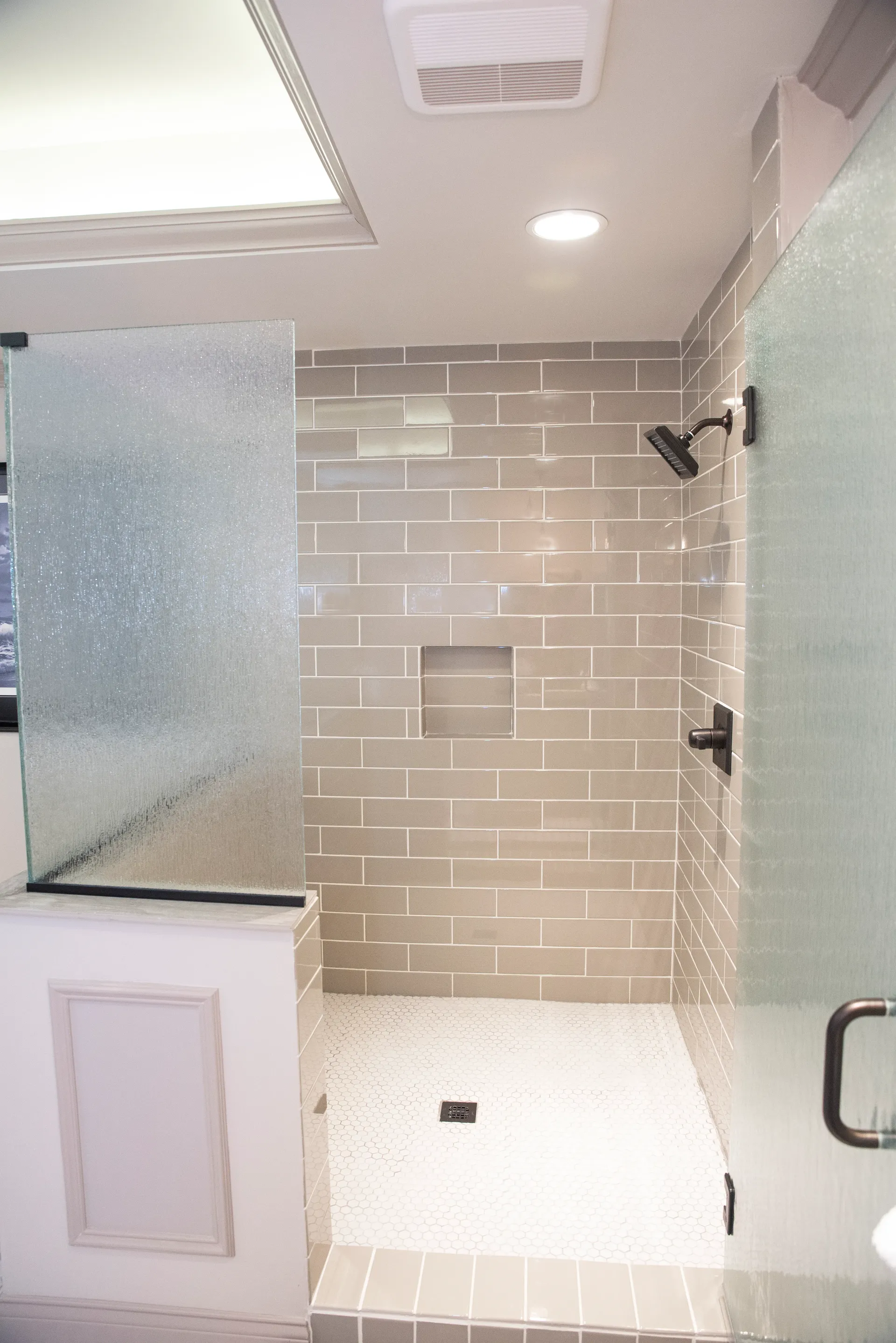 Modern bathroom with tiled shower stall, glass doors, and recessed shelf.