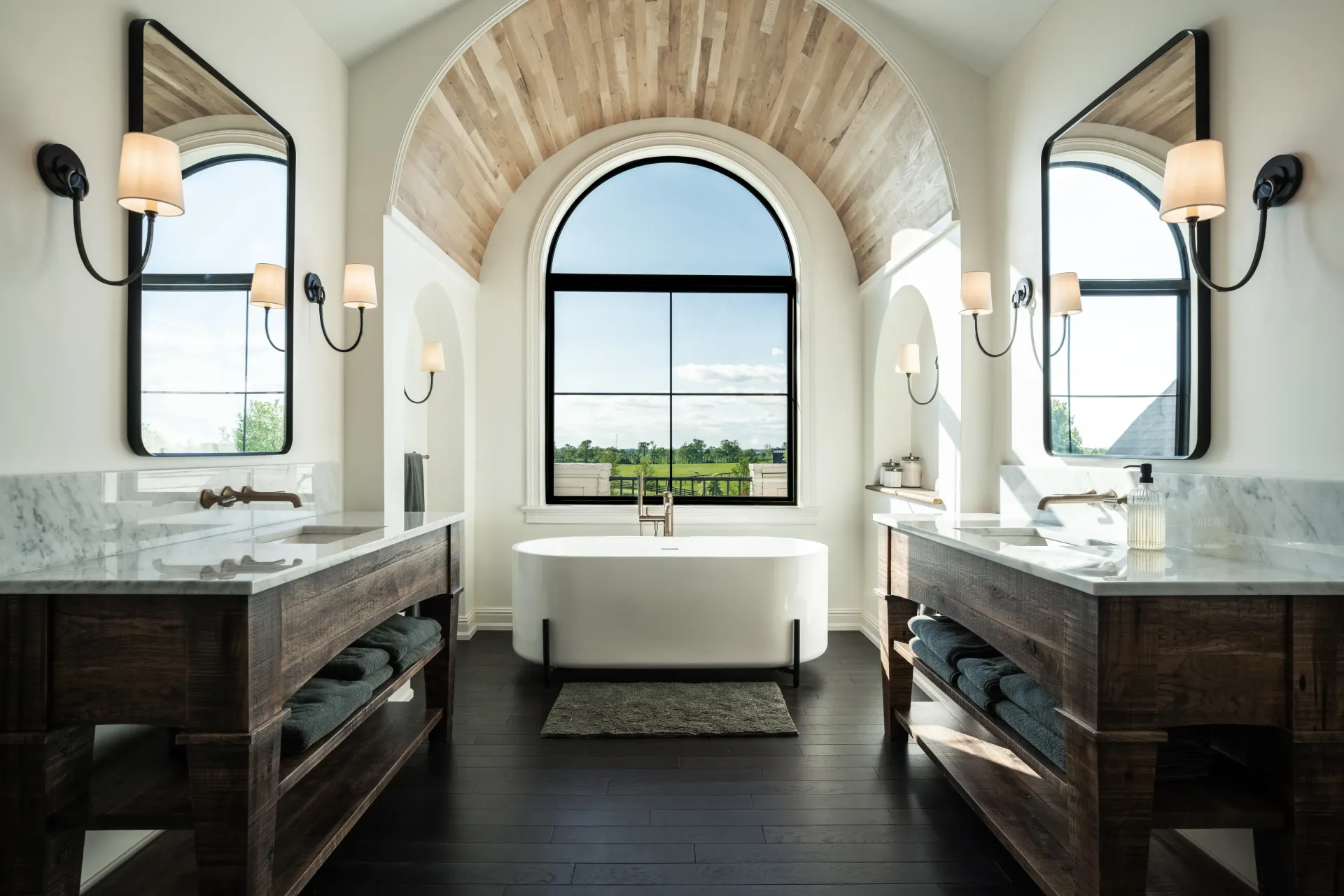 Bathroom with dark wood floors, white walls, arched window, and two wooden vanities with mirrors.