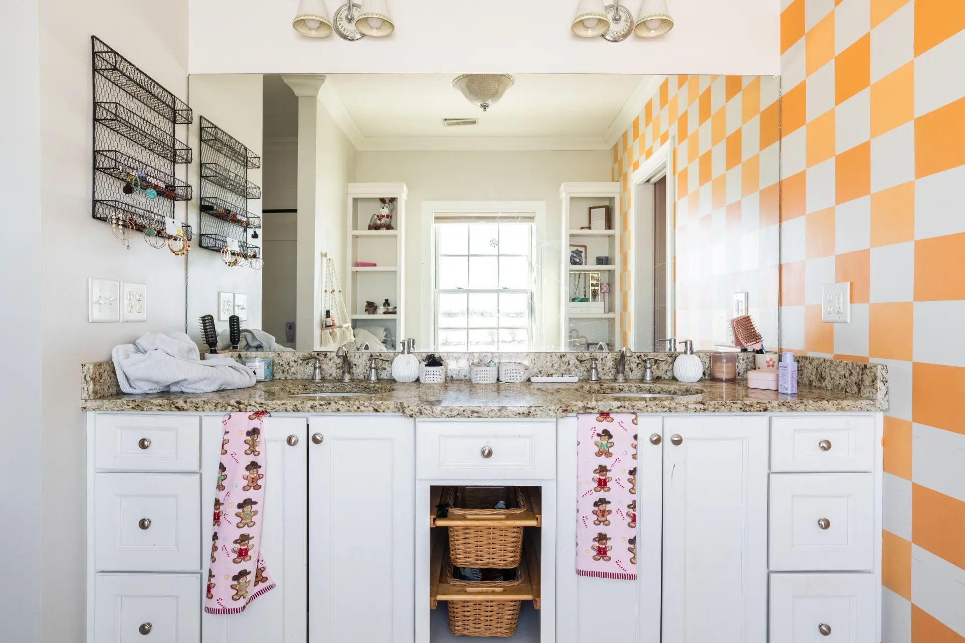 Bathroom with white cabinets, checkered orange wall, double sink, and large mirror.