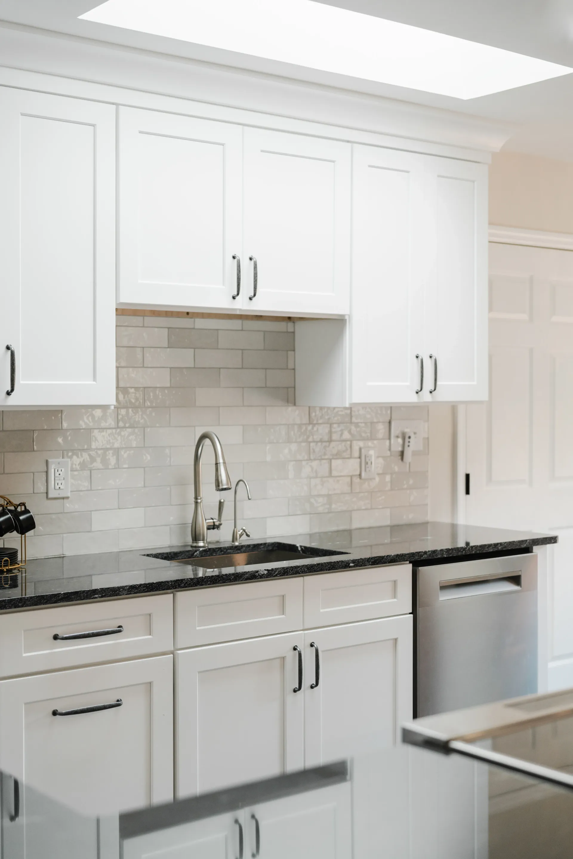 White kitchen cabinets with black countertops and stainless steel appliances.