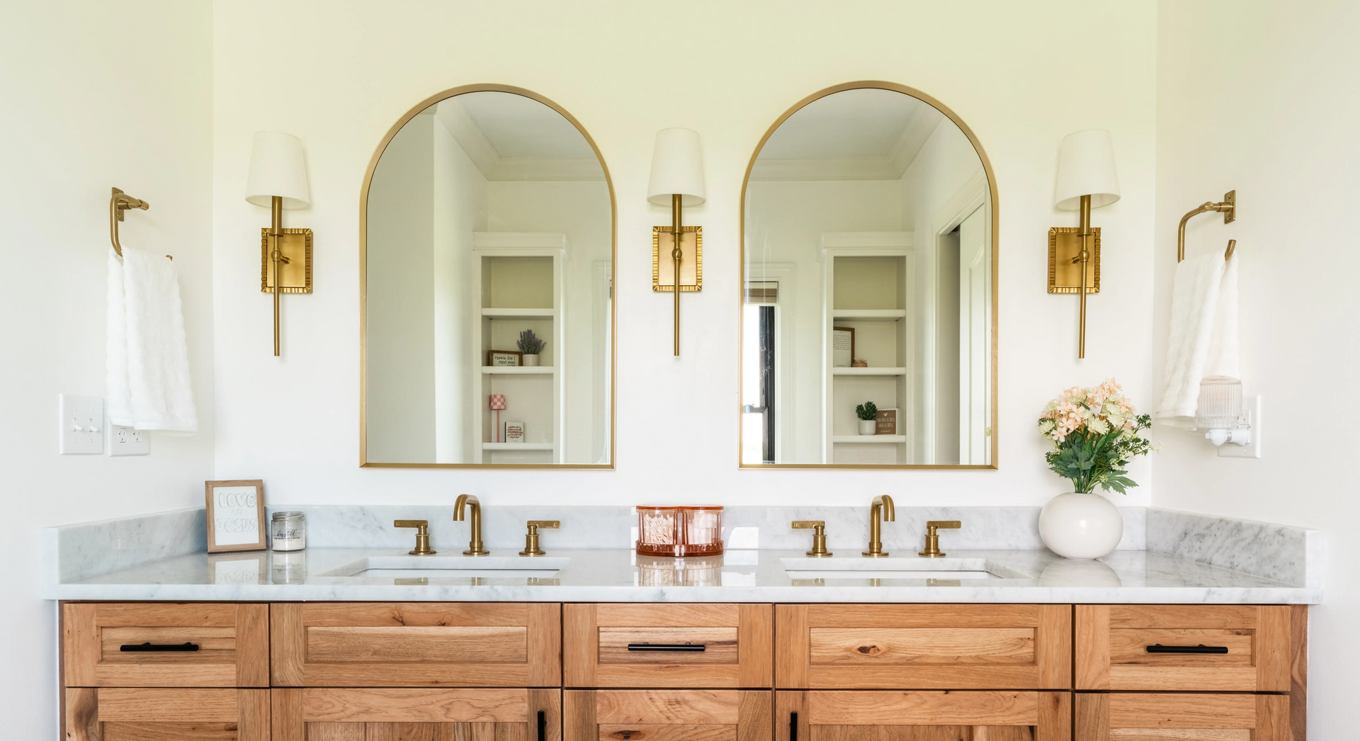 Bathroom with wooden vanity, two arched mirrors, gold fixtures, and marble countertop.