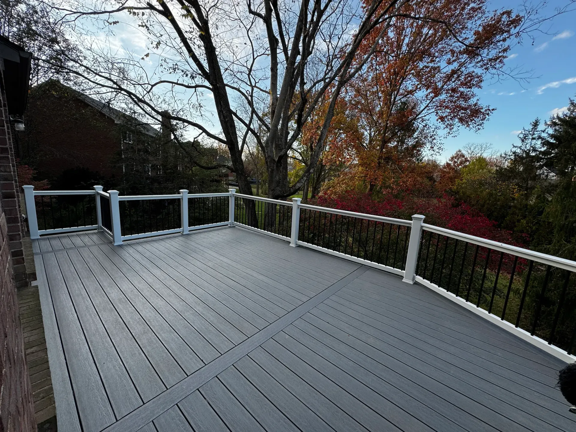 Grey composite deck with white posts and black railings, overlooking trees with fall foliage.
