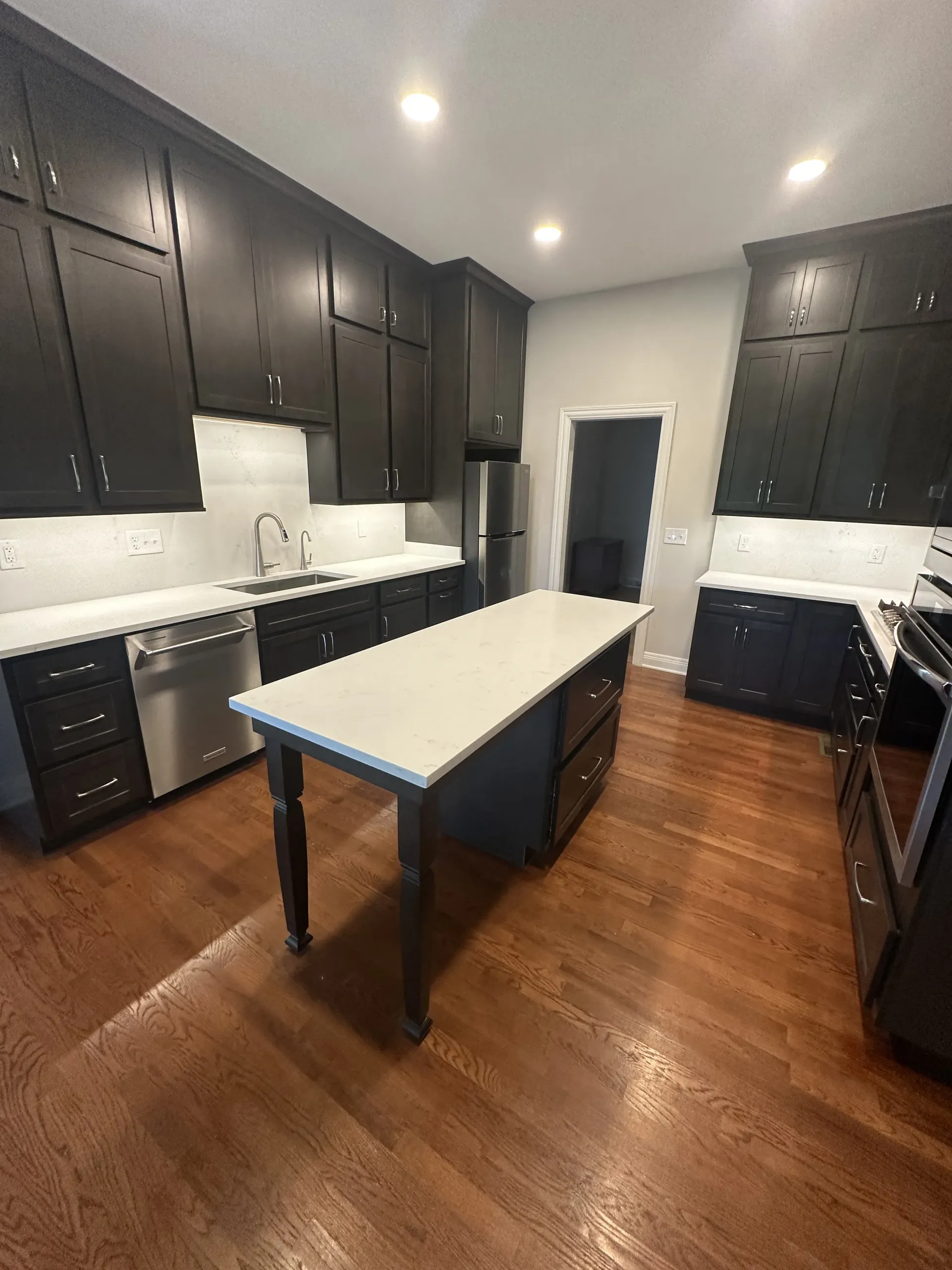 Modern kitchen with dark cabinets, white countertops, and a central island. Hardwood floors.