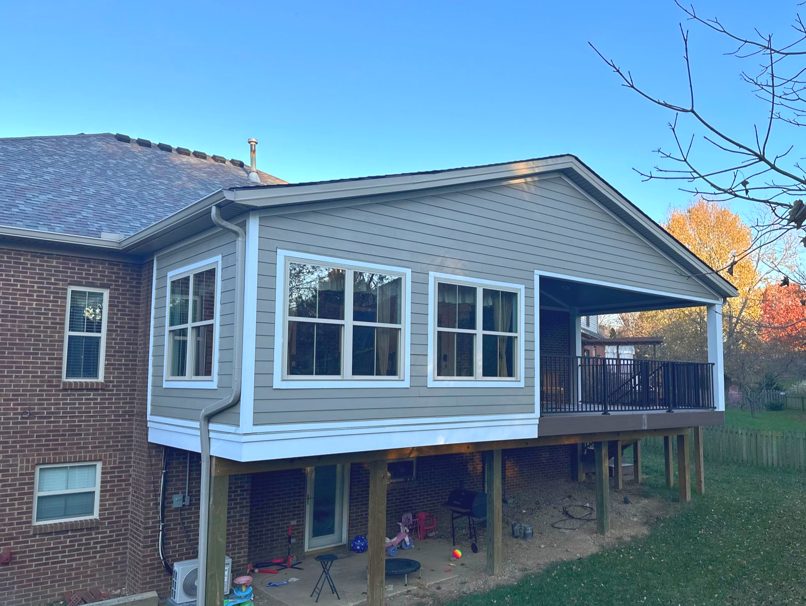 Sunroom addition with siding and windows, connected to a brick house and wooden deck.
