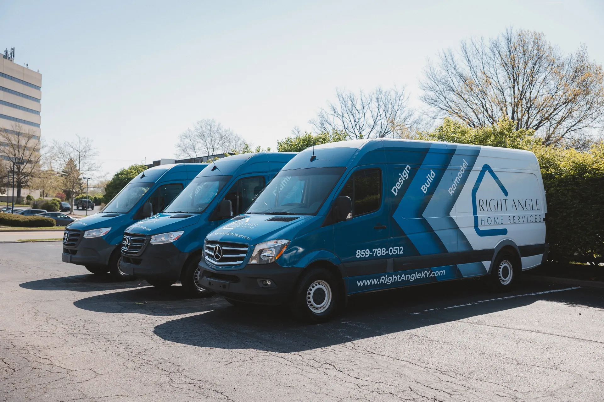 Three blue vans with company logo parked outside on a sunny day.
