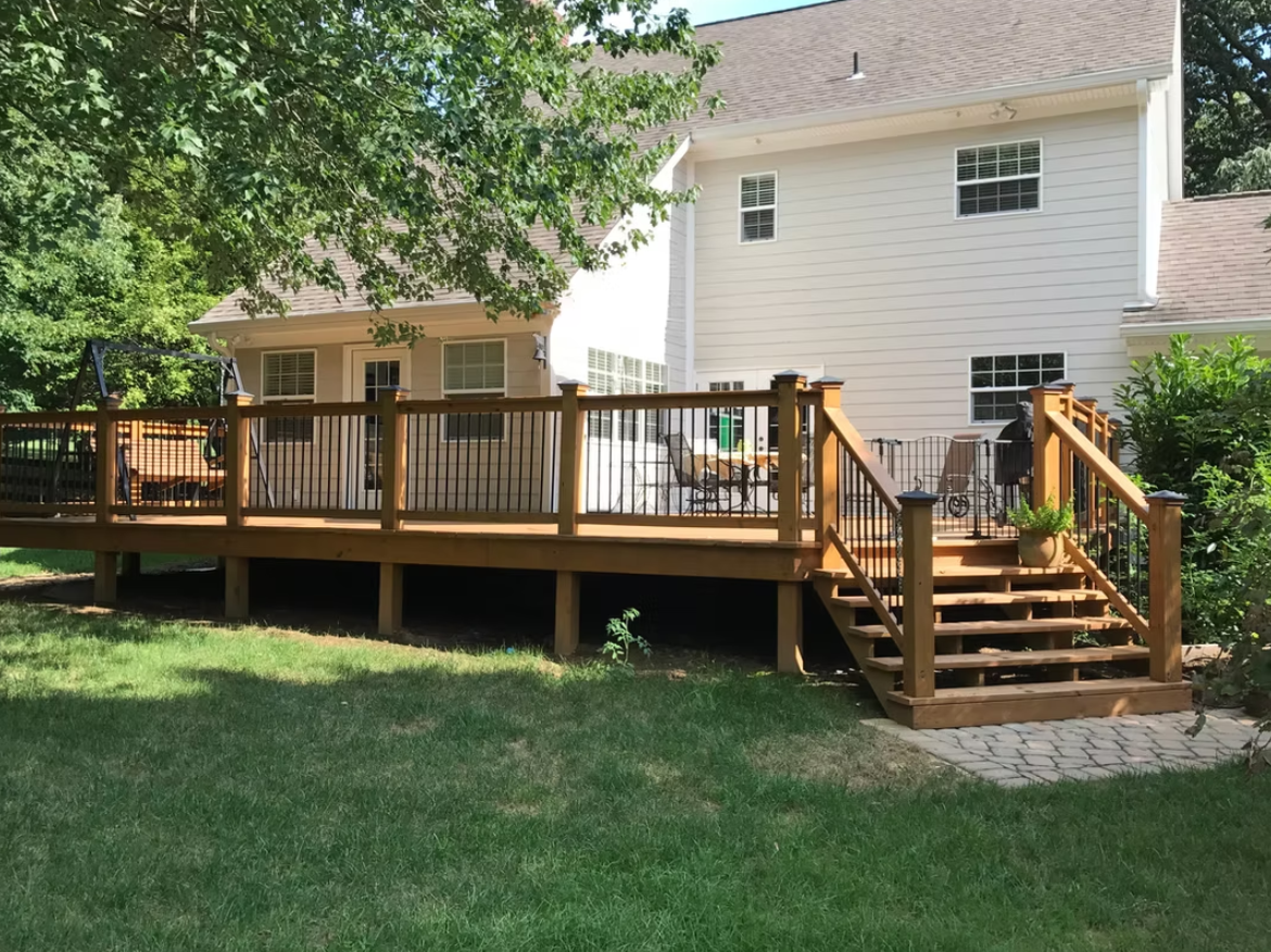Wooden deck with stairs attached to a two-story white house with green lawn.