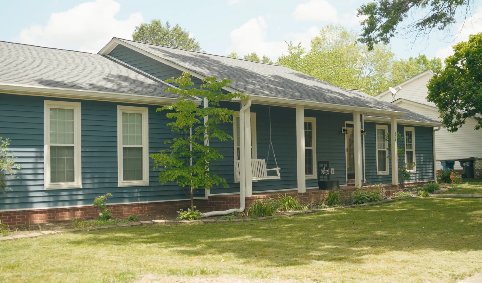 Blue house with white trim, porch, and a swing on a sunny day.