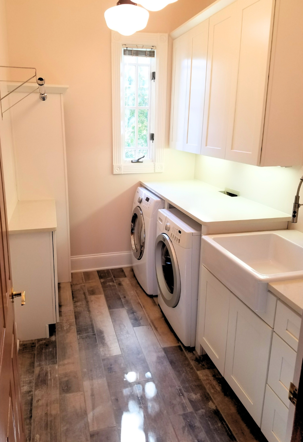 Laundry room with washer, dryer, sink, and white cabinets. Wood-look flooring and pink walls.