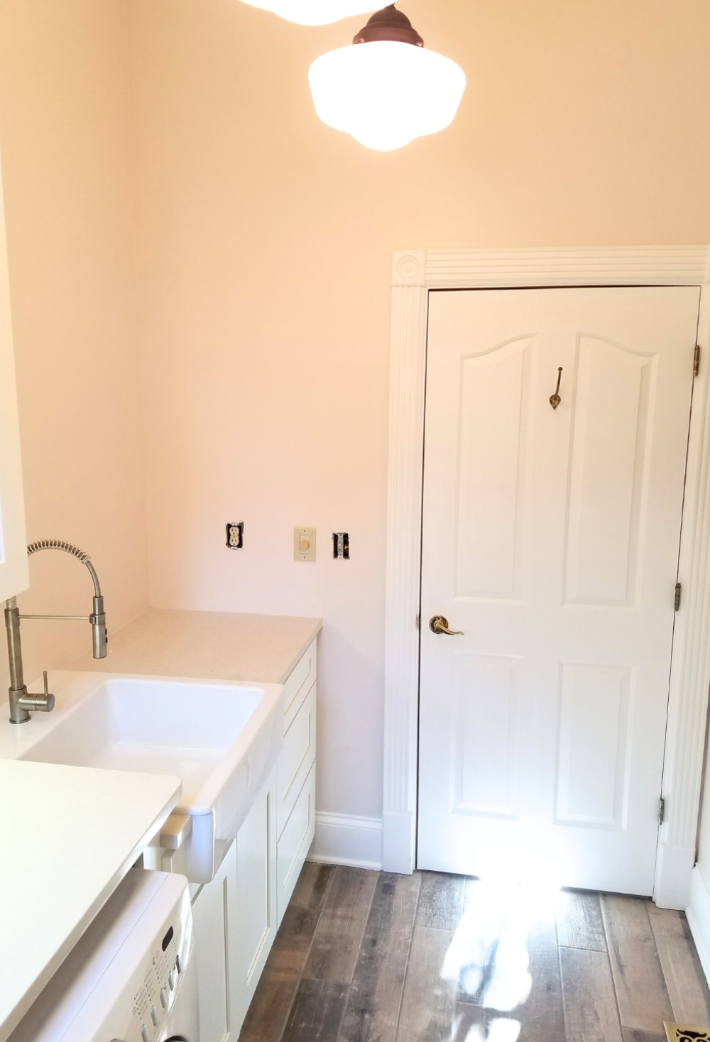 Kitchen with white sink, cabinets, and a door, pale pink walls, and wood floor.