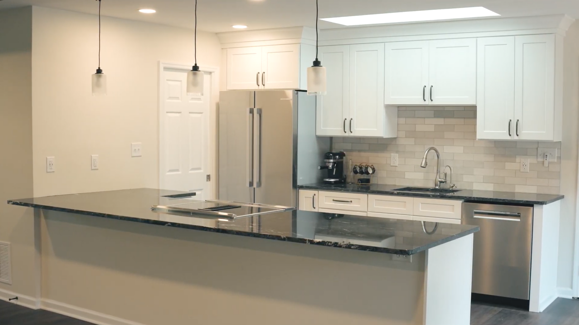 Modern kitchen with white cabinets, stainless steel appliances, dark countertop, and an island.