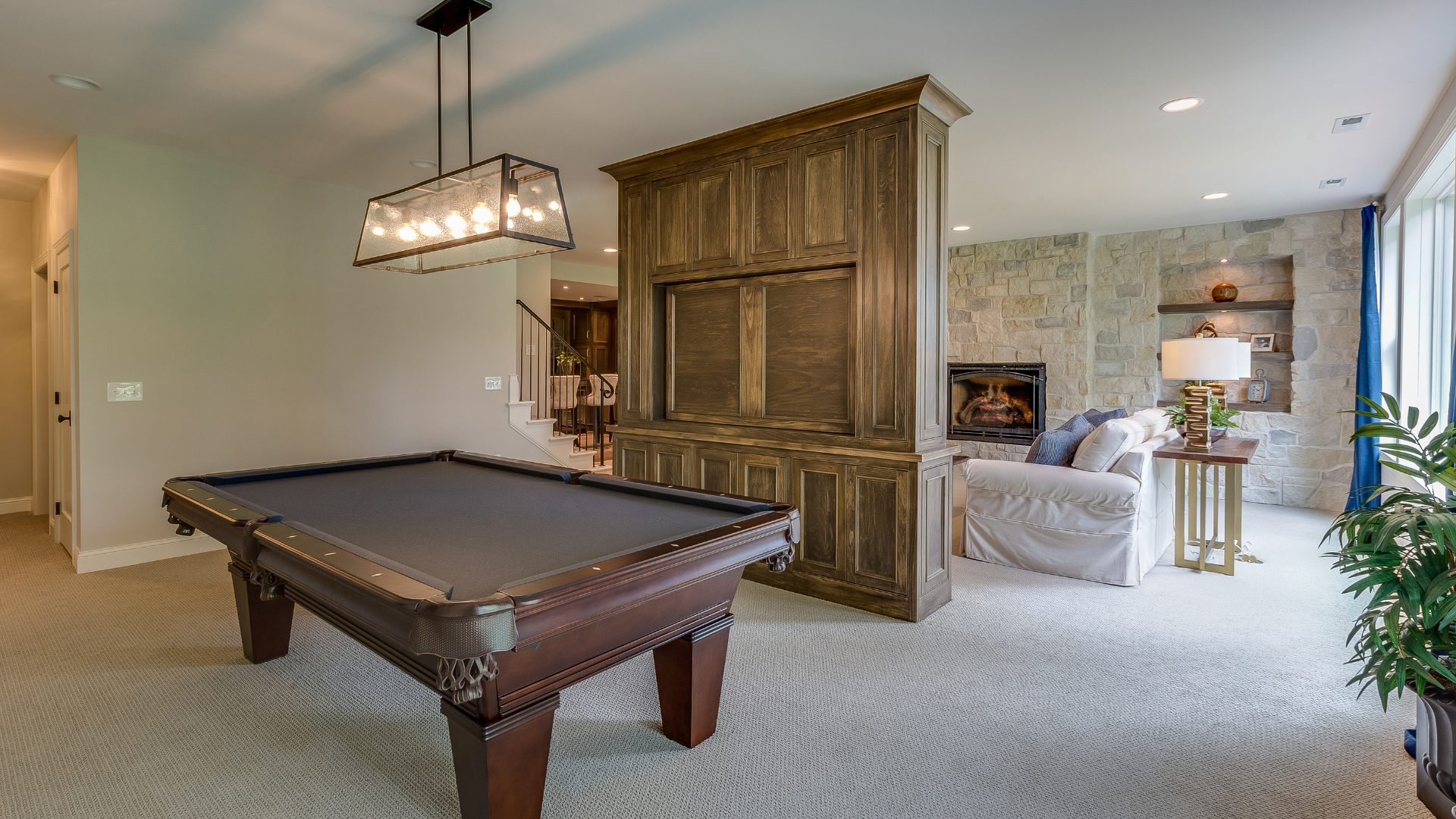 Game room with pool table, rustic wood cabinet, and seating area with fireplace. Beige carpet.