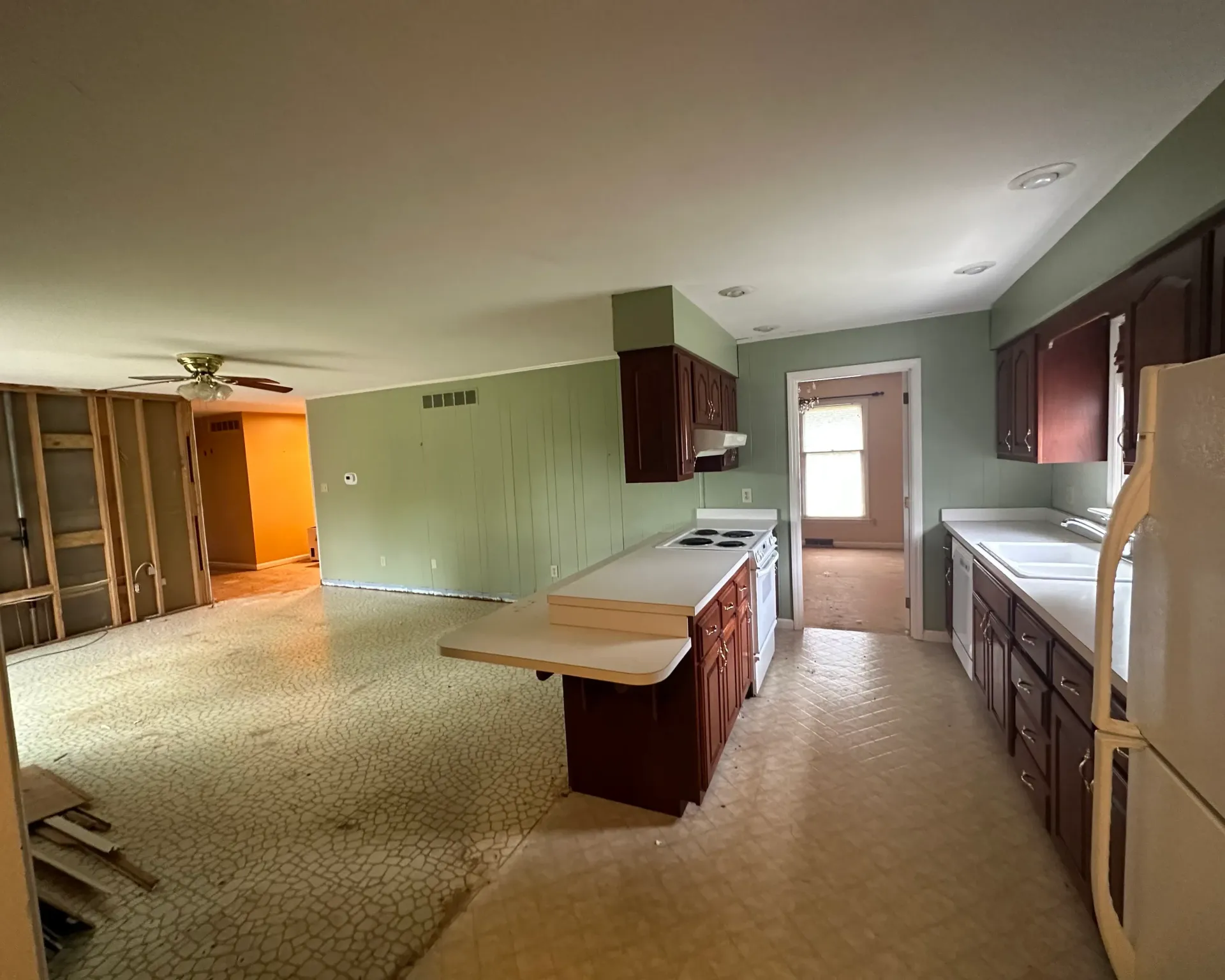 Kitchen with dark cabinets, white countertops, island, and appliances; green and tan walls; ripped up flooring.