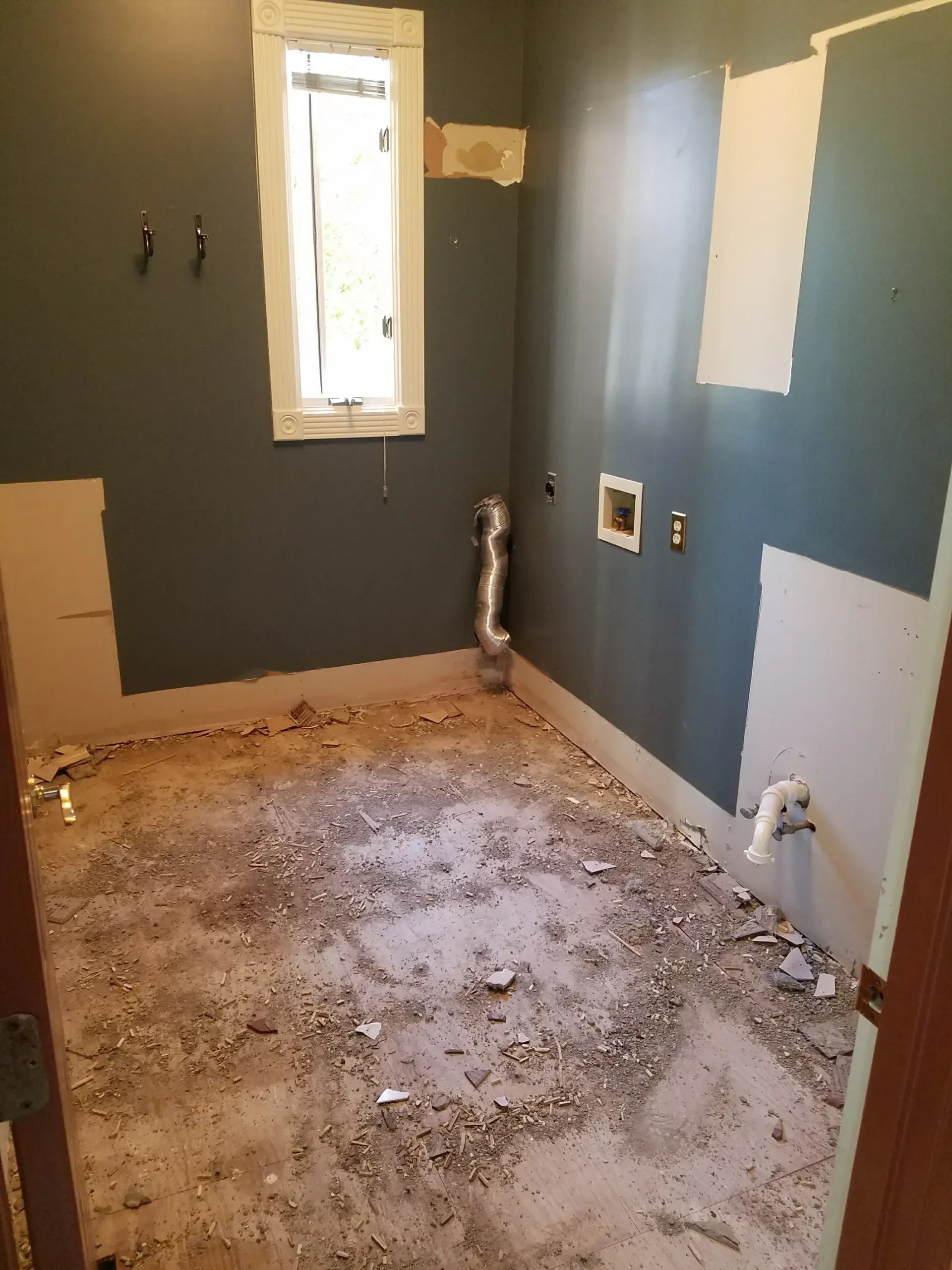 Laundry room renovation with exposed floor and drywall, dark blue walls, window.