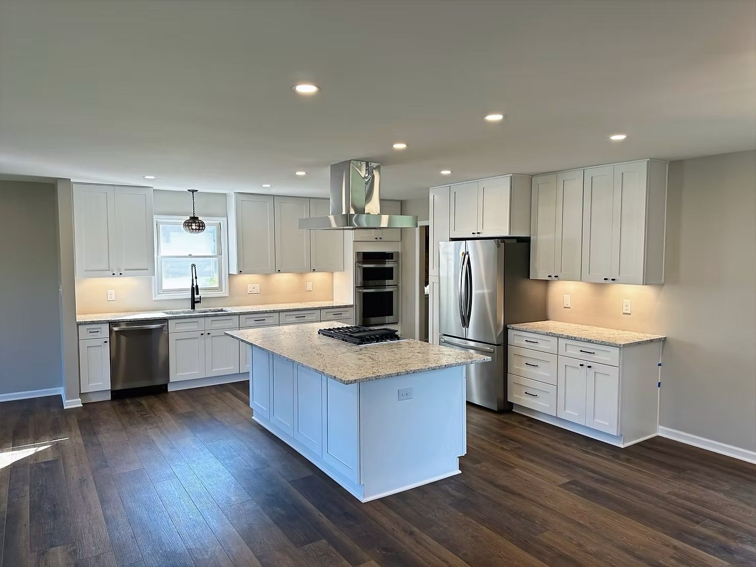 Modern kitchen with white cabinets, island, stainless steel appliances, and wood flooring.