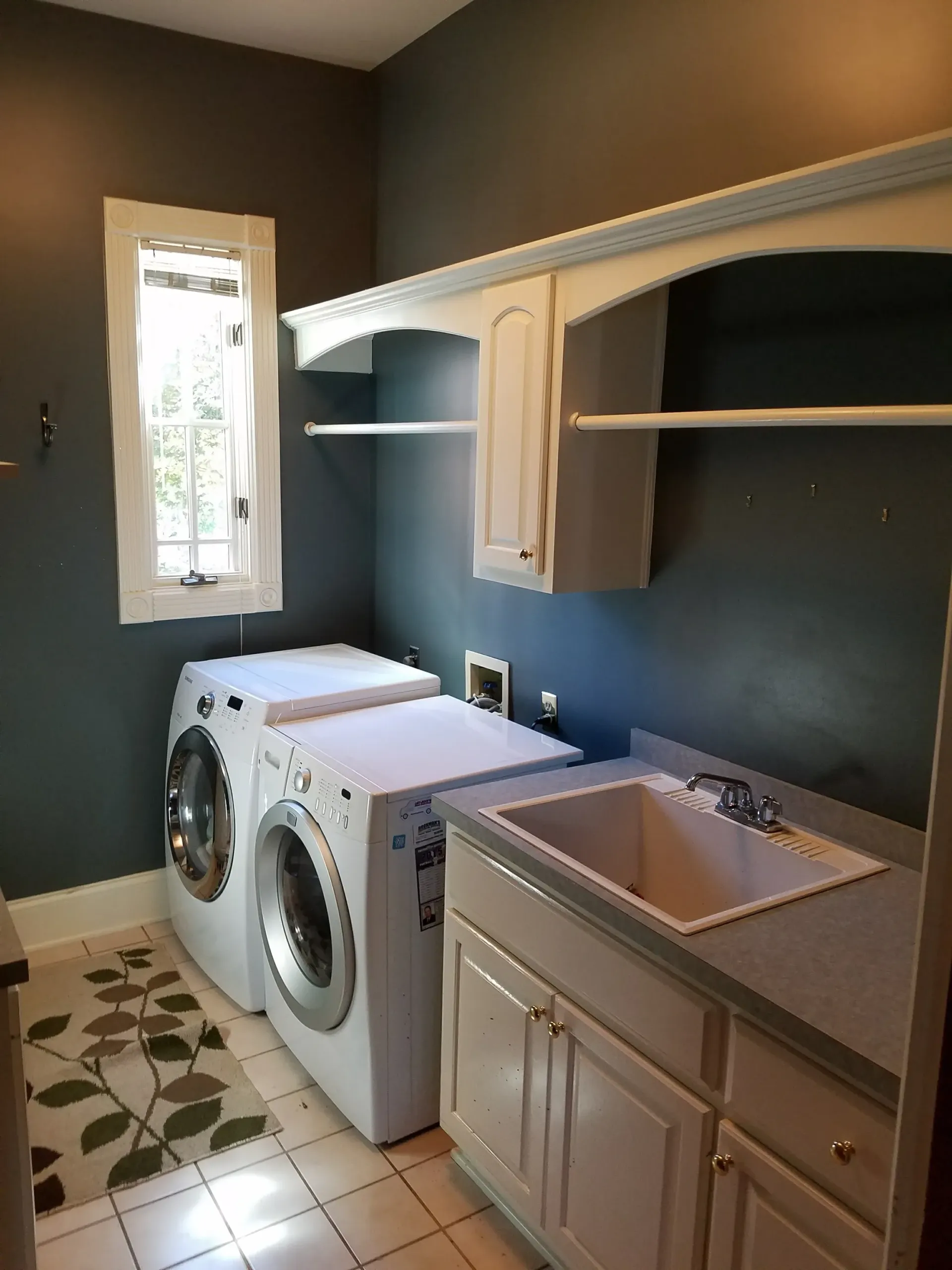 Laundry room with white appliances, sink, and cabinets against a dark blue wall.