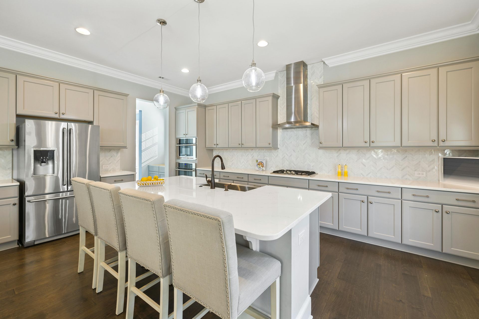 Modern kitchen with gray cabinets, white countertops, stainless steel appliances, and a central island with bar stools.