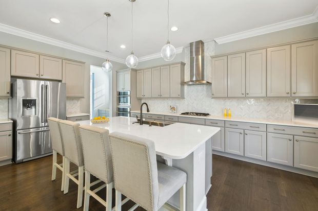 Modern kitchen with gray cabinets, white island, stainless steel appliances, and dark wood floors.