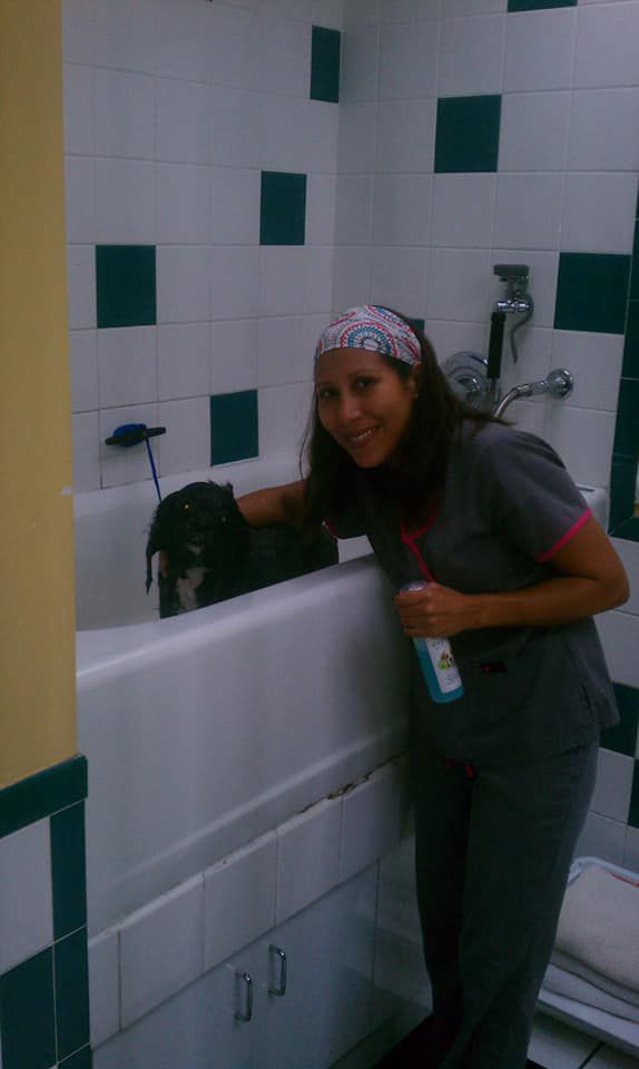 A woman is standing next to a bathtub with a dog in it.