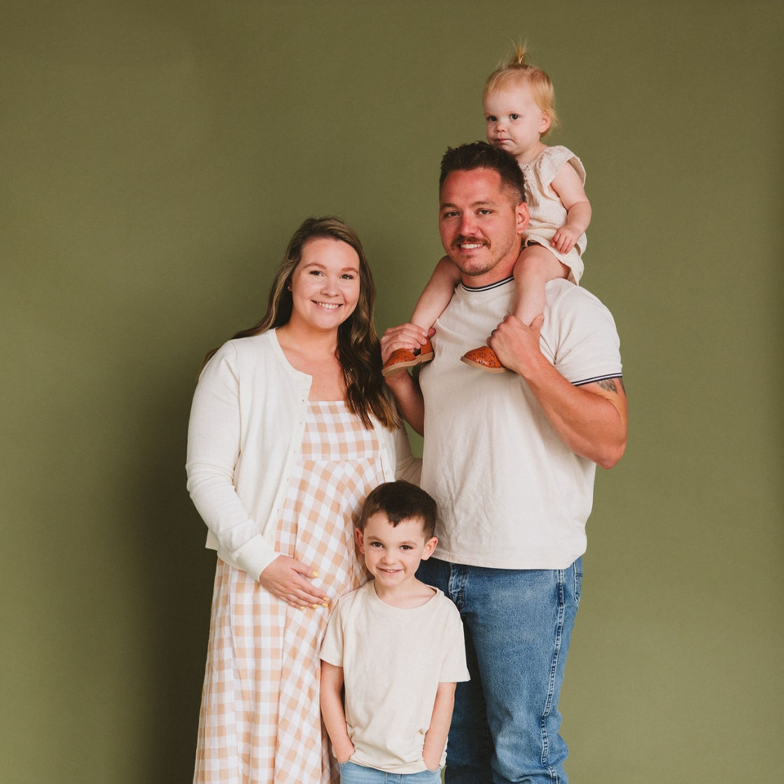 A man is holding a baby on his shoulders while standing next to a pregnant woman and two children.