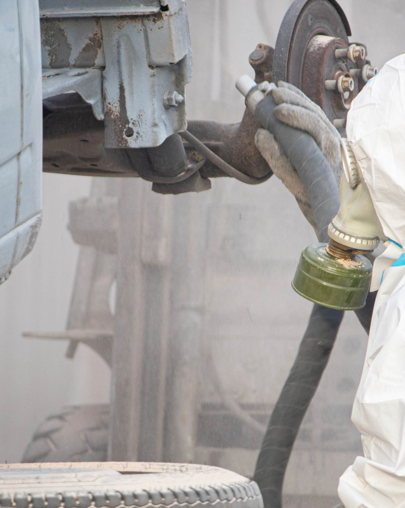 Person in protective suit and gas mask working on a vehicle; obscured by dust.