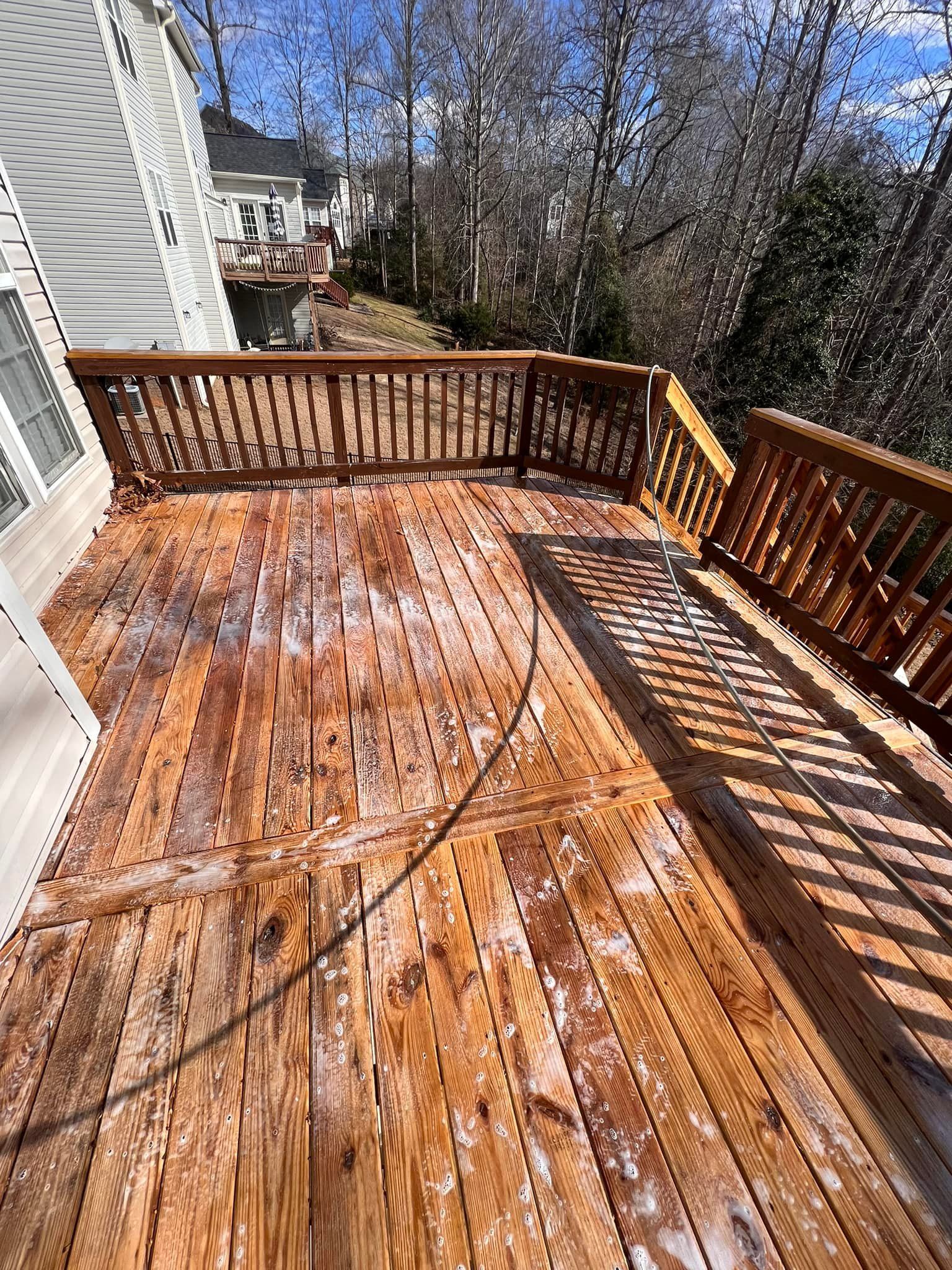 Wooden deck with visible weathering; brown railings and surrounding trees; sunny day.
