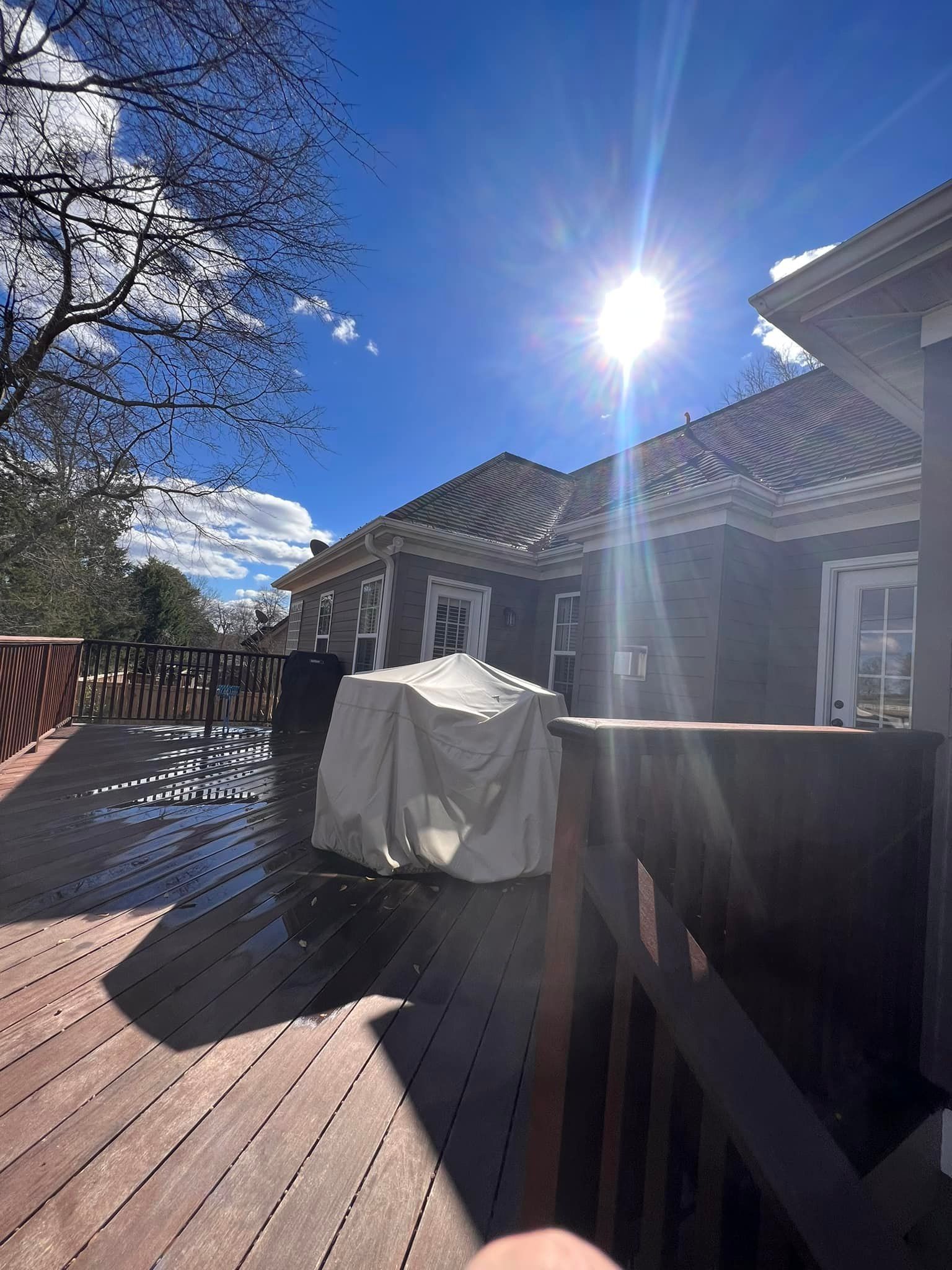 Sunny day on a wooden deck with a covered object and a house in the background.