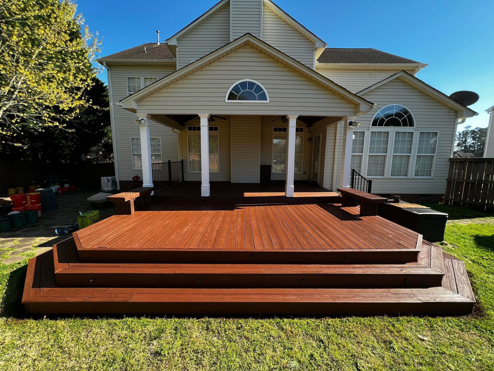 Backyard deck with steps, stained reddish-brown wood, leading to a covered porch with white columns. Beige house in background.