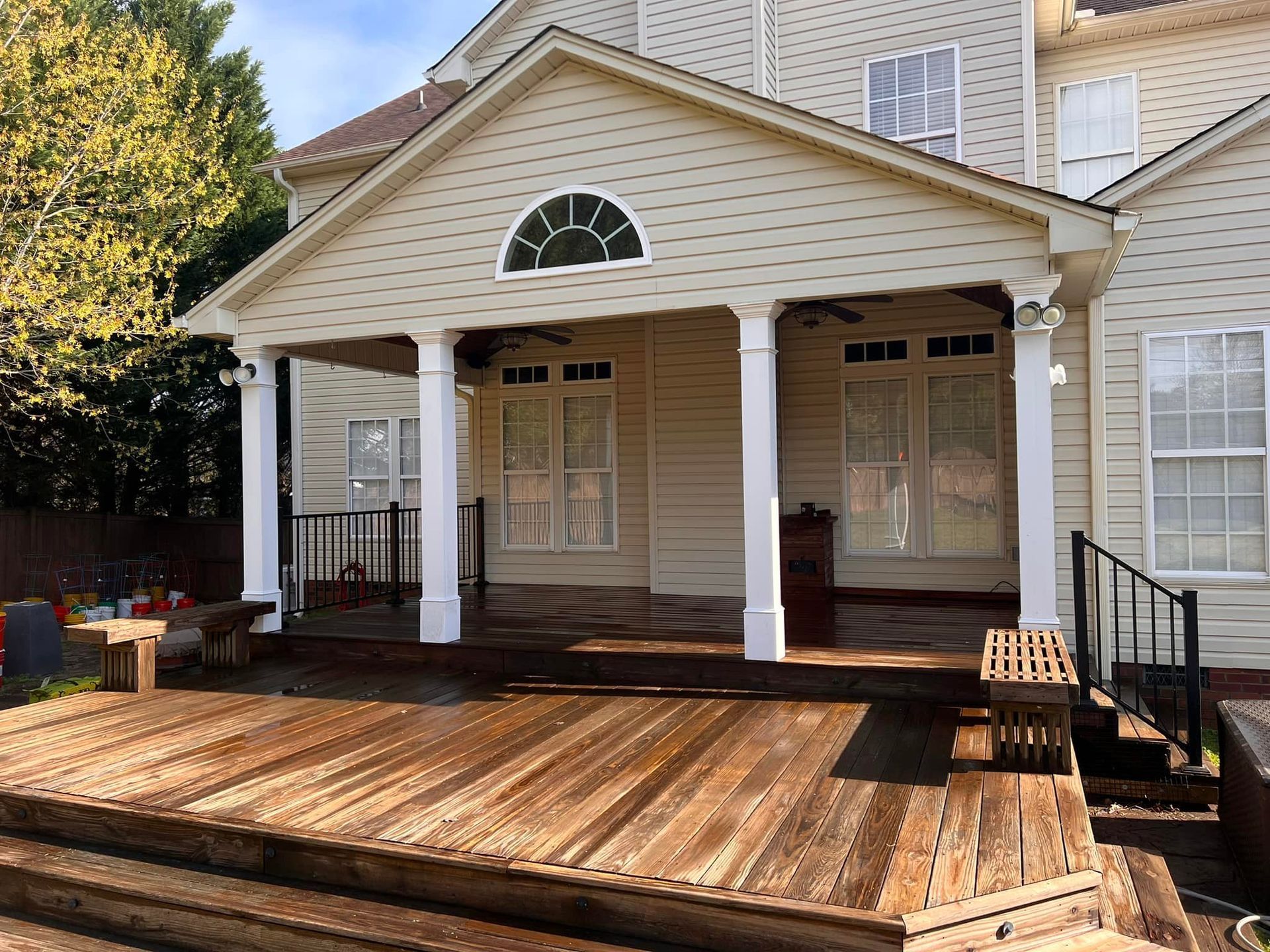 Wooden deck with covered porch, white columns, tan house, and trees.